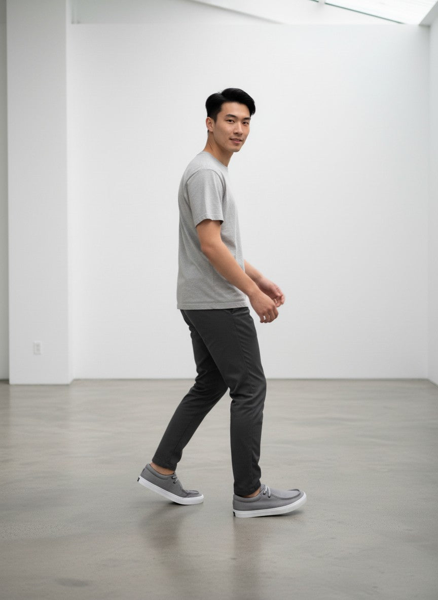 Hombre caminando con tenis CORE FOOTWEAR de lona gris y suela blanca en estudio minimalista